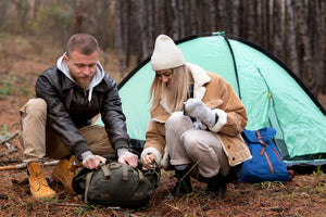Two people camping in a forest with a green tent and backpacks.